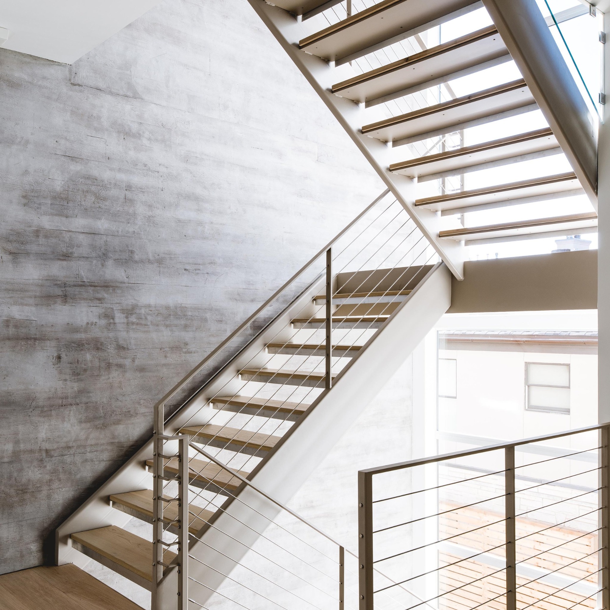 Open stair with metal cable railings and concrete wall