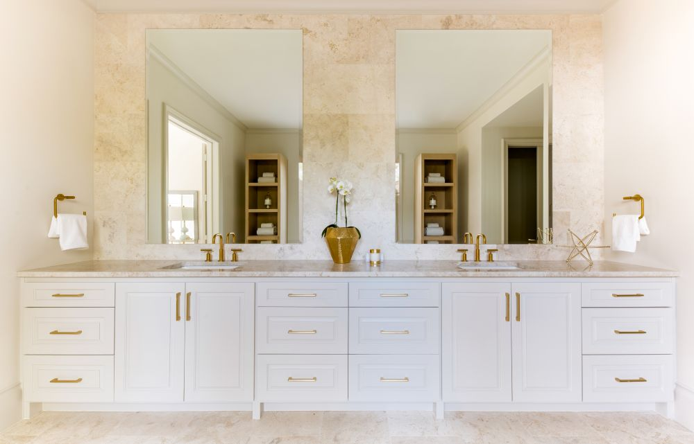 White double vanity with brass fixtures and stone backsplash
