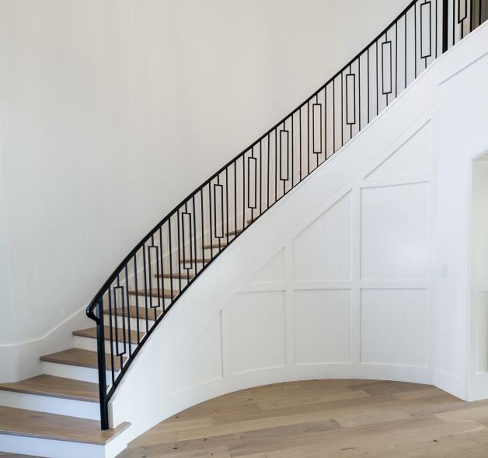 Curved stair with white paneled wall and iron railing